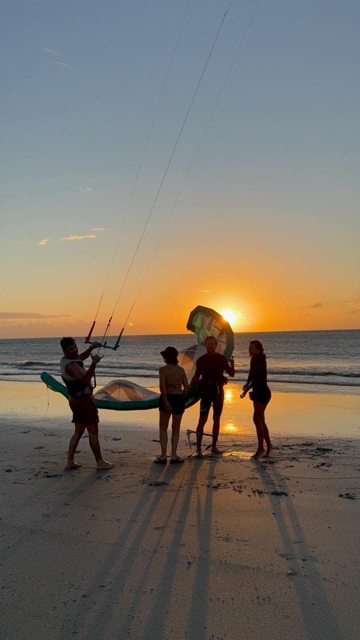 Groupe posant un kite sur la plage au coucher du soleil